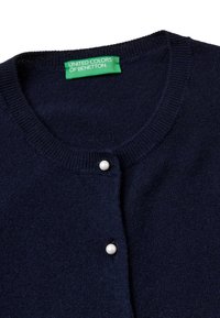 Granatowy sweter z dzianiny z perłowymi guzikami i zieloną metką United Colors of Benetton wewnątrz kołnierza.