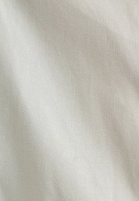 Tissu texturé gris clair avec un motif tissé subtil et des plis doux créant des ombres délicates sur la surface.