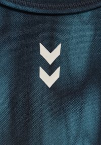 Niebieska tkanina o gradientowym kolorze z dwoma skierowanymi do góry białymi symbolami w kształcie szewronów, podkreślająca fakturowaną powierzchnię i kontrastowe elementy wzornicze.