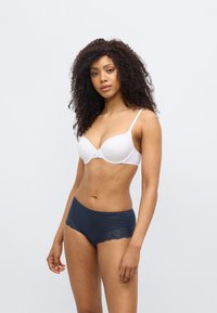 Λευκά σουτιέν με ρυθμιζόμενους ιμάντες και μικρή λεπτομέρεια φιόγκου, συνδυασμένα με σκούρα μπλε εσώρουχα hipster με λεπτομέρειες από δαντέλα.