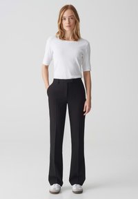 Pantalons noirs ajustés avec une coupe droite, associés à un haut blanc ajusté à manches courtes, avec une texture lisse et un look minimaliste.