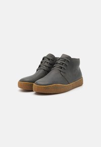 Botas de piel gris hasta el tobillo con puntera redonda, cordones en la parte delantera y suela de goma marrón texturizada. Presenta una superficie suave y un diseño minimalista.