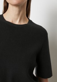 Schwarzes, geripptes Strickshirt mit kurzen Ärmeln und rundem Ausschnitt, das eine glatte Textur aufweist. Keine sichtbaren Muster oder Hardware-Details.