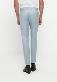 Pantalons ajustés bleu clair présentant une coupe slim, une texture lisse, et un détail de poche arrière, associés à des bottines noires.