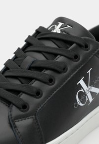 Zapatilla negra de cuero con cordones planos, con una suela de goma blanca y un discreto logo "Calvin Klein Jeans" en el lateral.
