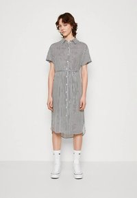 Svītraina kleita ar pogām priekšā, īsām piedurknēm, josta viduklī, ceļgala garuma apakšmala, izgatavota no viegla auduma melnā un baltā krāsā.