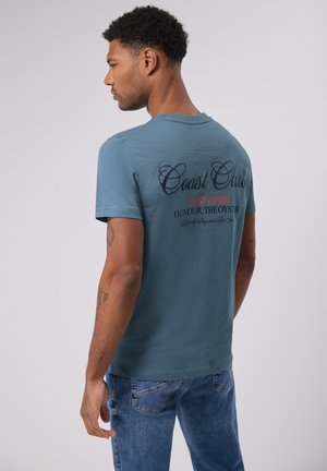 Lichtblauwe katoen T-shirt met korte mouwen. Heeft "Coast Club" in donkere letters en "Finest Seafood" in rood, met aanvullende tekst hieronder.