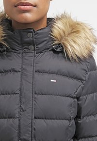 černá péřovka s kapucí z umělé kožešiny, s komfortním zipem a patentkami. Materiál vypadá hladce a je prošívaný.