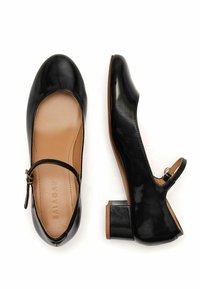 Zapatos de charol negros de tacón bajo con punta redondeada, correa para el tobillo y interior beige, que cuentan con un tacón cuadrado y una textura suave.
