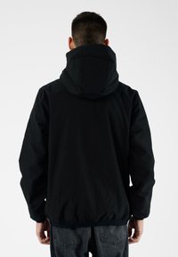 Giacca nera con cappuccio, colletto alto, polsini elasticizzati e orlo sfiancato. Texture liscia, design minimalista senza loghi o motivi visibili.