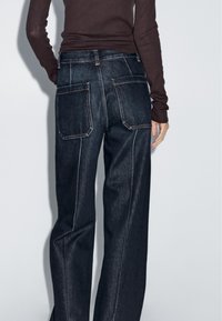 Dark wash denim jeans with a straight-leg cut, highlighted stitching, and two large back pockets. No front view visible.