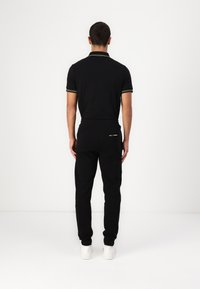 Schwarzes Polo mit gelben Akzenten und schwarzen Jogginghosen. Das Outfit hat eine lockere Passform und wird mit weißen Sneakers kombiniert.