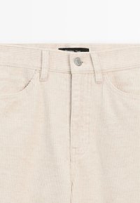 Light beige corduroy pants with vertical ribbing, featuring a button closure, belt loops, and a front pocket.