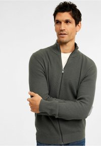 Grå ribbade zip-up-tröja med hög krage och långa ärmar, med en texturerad tyg och dragkedja framtill.