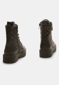 Botas de tobillo acolchadas de cuero negro con un tacón grueso, cremallera lateral y suela de goma negra. Cuenta con un upper texturizado y una pestaña para tirar.