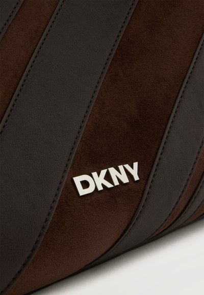 Близък план на кафява велурена и тъмна кожена чанта със сребристо лого DKNY отпред.
