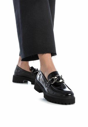Mocasines de charol negro con suelas gruesas, con un acento metálico decorativo en forma de cadena. Acabado texturizado y tacón ligeramente elevado.