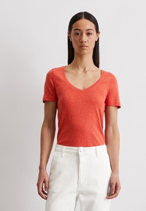 T-shirt à manches courtes, col en V, de couleur corail unie, en tissu léger et texturé, associé à un pantalon blanc taille haute.