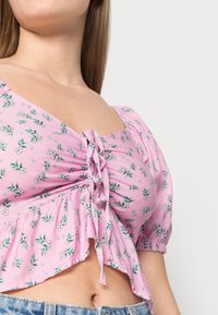 Růžový květinový crop top s krátkými puff rukávy, detailem s nařaseným předním dílem a volánovým lemem, vyrobený z lehkého materiálu.