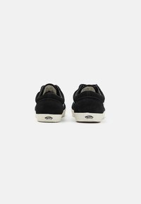 Sneaker nere in suede con profilo basso, dotate di una suola in gomma bianca e dettaglio del logo sul tallone. La vista posteriore mette in evidenza i dettagli cuciti.