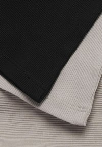 Zložena rebrasta tkanina v črni in bež barvi, ki poudarja šivane robove in teksturiran pleteni vzorec.