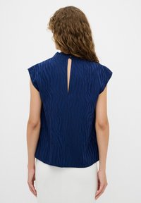 Blusa blu navy con maniche a cappotto, motivo zebramato testurizzato, dettaglio a chiave sul retro e vestibilità morbida. Realizzata in tessuto leggero.