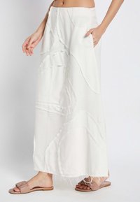 Weißer Leinen-Maxi-Rock mit schichtartigem, abstraktem Patchwork-Design und rohen Kanten. Verfügt über seitliche Taschen und einen lockeren Schnitt. Getragen mit beige flachen Sandalen.
