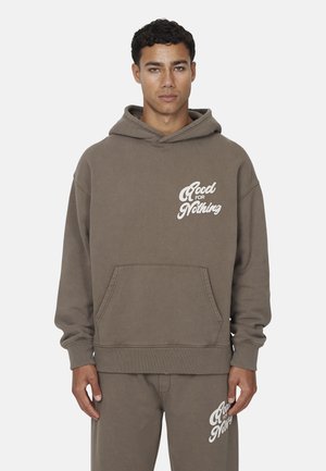 Haut à capuche en coton brun avec une poche kangourou et des poignets côtelés, arborant le texte blanc "Good for Nothing" sur la poitrine. Assorti avec un pantalon de survêtement coordonné.
