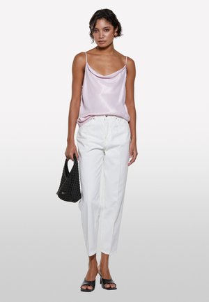 Camicetta in satin rosa chiaro con spalline sottili, abbinata a pantaloni bianchi a vita alta, borsa intrecciata nera e décolleté neri.