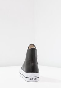 Mustat nahkaiset korkeavartiset lenkkarit, joissa on valkoinen kumipohja, mustat tikkaukset ja pyöreä logo-ompelus ulkopuolella. Minimalistinen muotoilu.