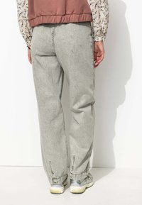 Pantalons en denim gris clair avec une coupe décontractée, featuring une jambe fuselée et des poignets élastiques. Assortis à des chaussures de sport grises.