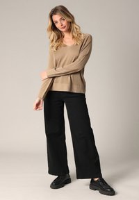 Beige, lange mouwen gebreide trui met een V-hals, gecombineerd met wijde zwarte broeken en zwarte veterschoenen. Glad textuur, casual fit.