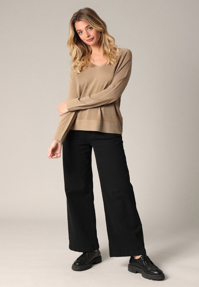 Beige, lange mouwen gebreide trui met een V-hals, gecombineerd met wijde zwarte broeken en zwarte veterschoenen. Glad textuur, casual fit.