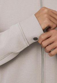 Light gray jacket featuring a smooth texture, a zip closure, and a button accent on the cuff, highlighting its modern design.