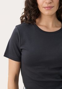 Tamno siva kratka majica s kratkim rukavima, okruglim izrezom i mekom, glatkom teksturom. Ima prilagođeni oblik i suptilne detalje šivanja.