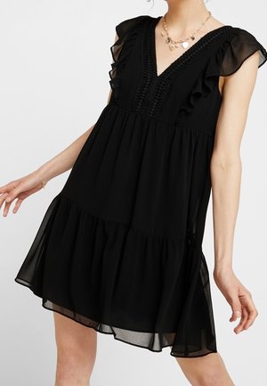 Schwarzes, fließendes Kleid mit Rüschenträgern, einem V-Ausschnitt und einem gestuften Rock. Verfügt über filigrane Stickereien auf dem Oberteil.