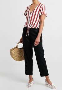 Červeno-bílý pruhovaný krátký rukáv top s V-výstřihem a zavazováním vpředu, zkombinovaný s černými úzkými kalhotami. Pletená taška a bílé perforované boty.