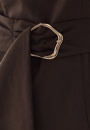 Cinturón de tela marrón con una hebilla de plata de forma irregular y textura suave, asegurada por un lazo de tela.