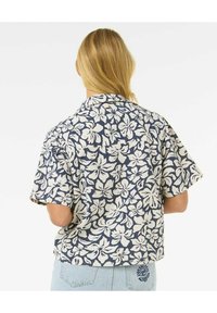 Kurzarmhemd in Marineblau mit weißem Blumenmuster, ausgestattet mit einem eingeprägten Kragen und lässiger Passform. Detail auf der Rückseite umfasst ein kleines gesticktes Logo.