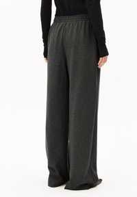 Schwarz-graue weite Hosen aus einem dunklen Stoff mit elastischem Bund und glatter Textur, von hinten präsentiert.