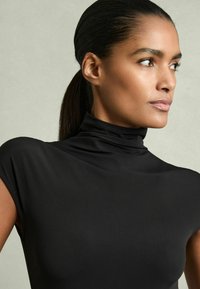 Kohandatud must turtleneck-särk lühikeste varrukatega, valmistatud pehmest kangast. Sile tekstuur kõrge kaelusega ja minimalistlik disain.