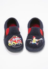 Marineblaue Fleece-Hausschuhe mit roten elastischen Seitenakzenten. Auf jeder Zehe sind gestickte Designs eines Feuerwehrautos und einer Figur mit einem Schlauch.