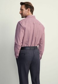 Czerwono-biała w kratę koszula z długim rękawem, z kołnierzykiem zapinanym na guziki oraz czarnym paskiem, w połączeniu z ciemnoszarymi spodniami o dopasowanym kroju.