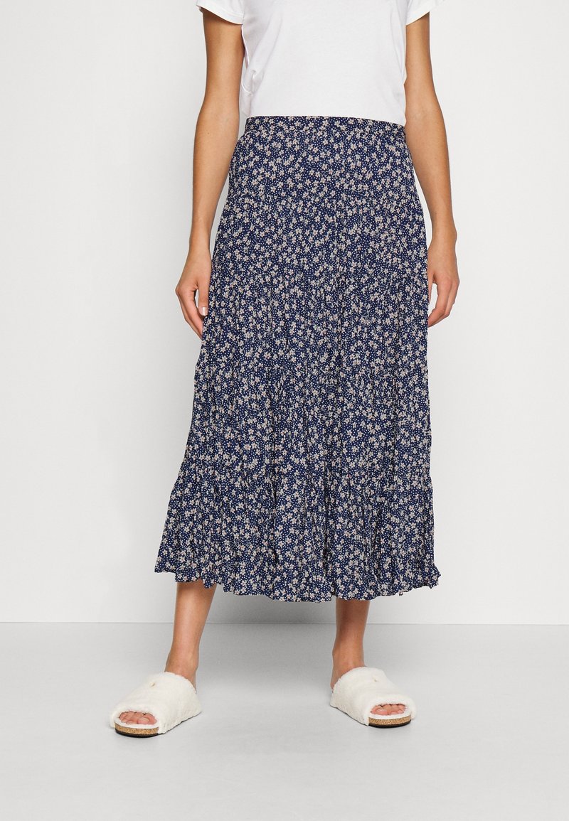 Jupe midi florale marine avec un ourlet à volants superposés et un petit motif de fleurs blanches. Portée avec un haut blanc uni et des sandales moelleuses.