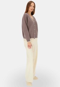Szary dziergany kardigan z dekoltem w kształcie V, z perłowymi guzikami. Połączony z beżowymi spodniami o szerokich nogawkach i beżowymi butami na slip-on.