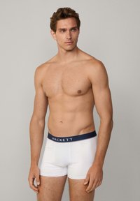 Boxer briefs bianchi con una cintura blu navy che presenta il nome del marchio "HACKETT." Tessuto liscio, design aderente e lunghezza fino a metà coscia.