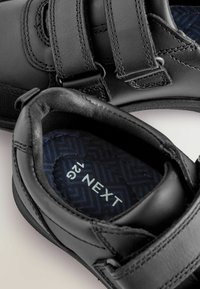 Scarpe nere con cinturini in velcro, finitura in pelle liscia, soletta blu testurizzata con motivo a spina di pesce, etichetta della misura "12" visibile.