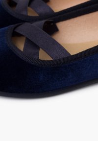 Bailarinas de terciopelo azul marino con tiras de satén cruzadas y un suave forro beige. Suelas de goma con bordes texturizados para mayor agarre.