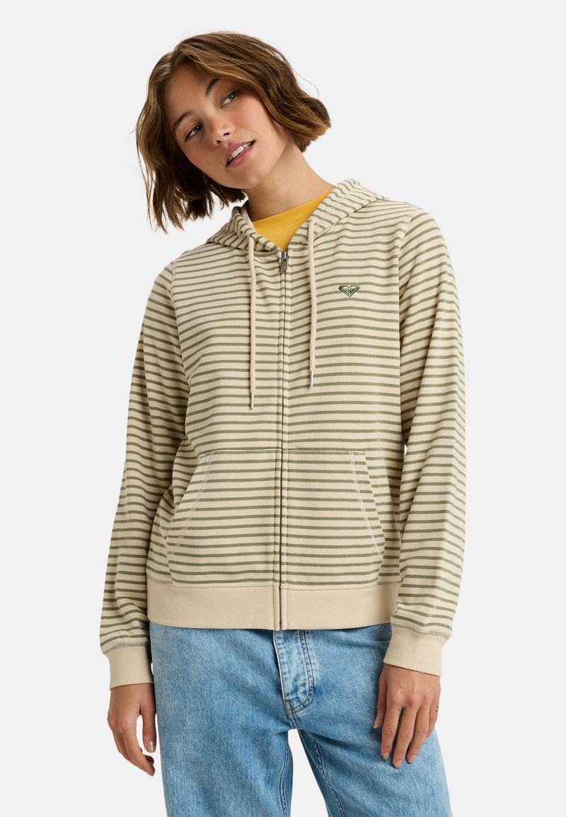 Sudadera cremosa con cremallera, rayas horizontales verdes, capucha con cordón, bolsillos tipo canguro y un pequeño logo en el pecho. Lleva puesta una camiseta amarilla debajo.