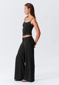 Black, wide-leg trousers with a smooth texture and pleated front, paired with a fitted black tank top. Designed for a relaxed fit.